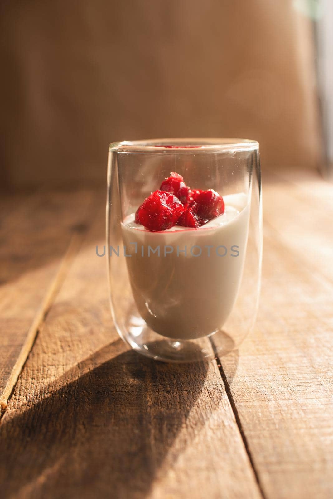 double glass with yogurt and berries on a wooden table where the bright sun is shining