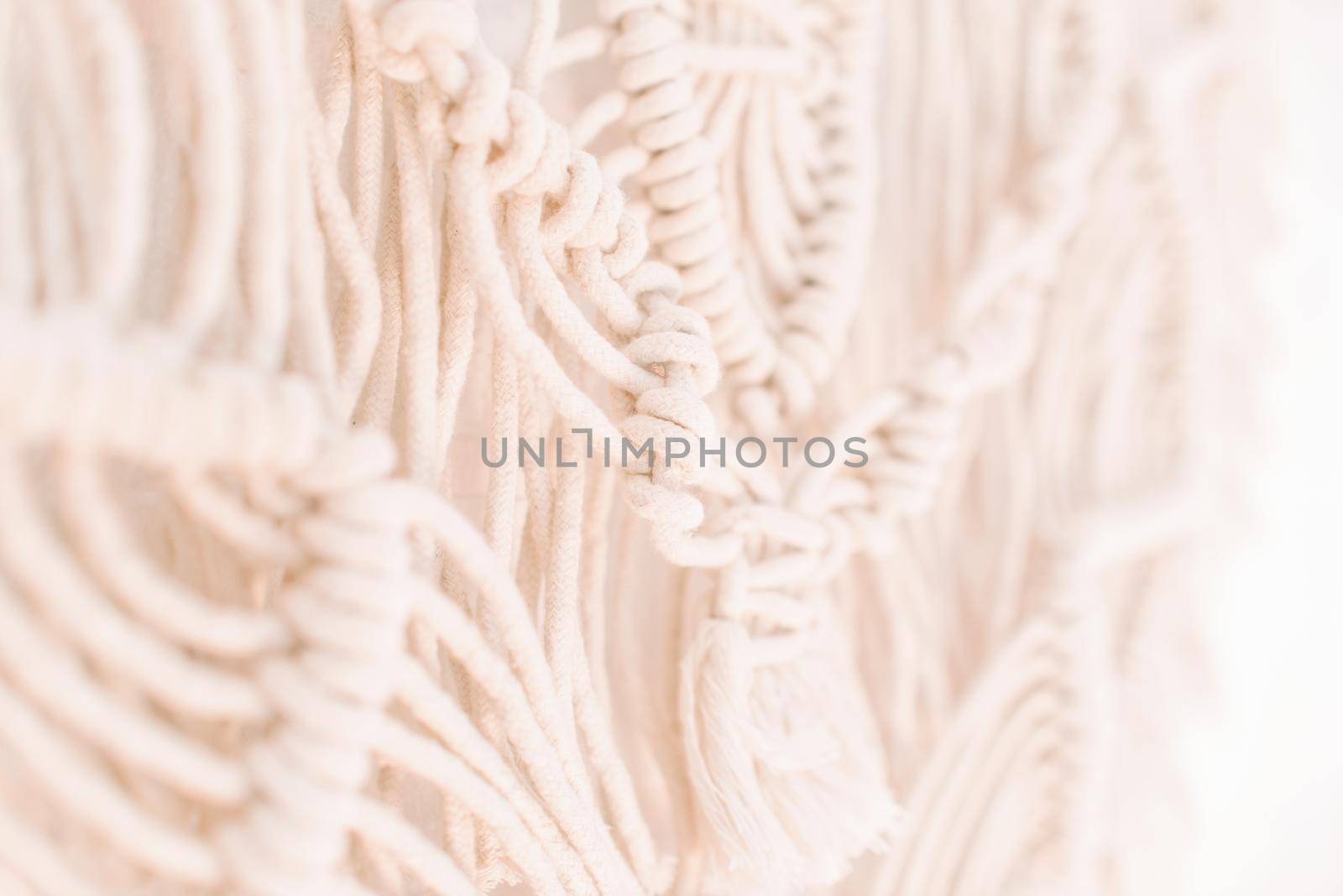 fragment of wall panel in boho style made of cotton threads of natural color using macrame technique for home and wedding decor.