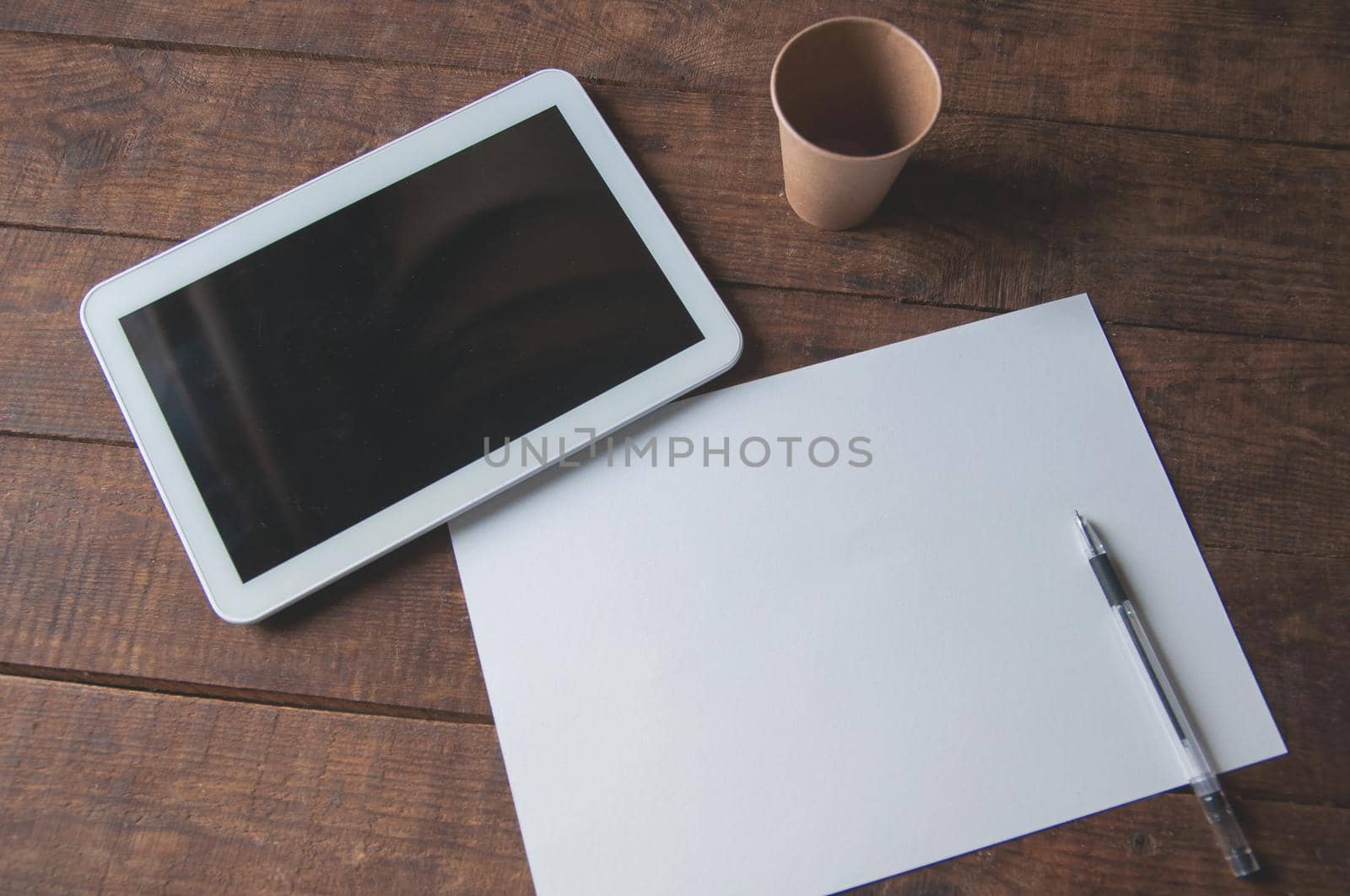 Office workplace with tablet pc on the table. On the table there is a tablet and a white sheet of paper with a pen. For a design presentation or portfolio.