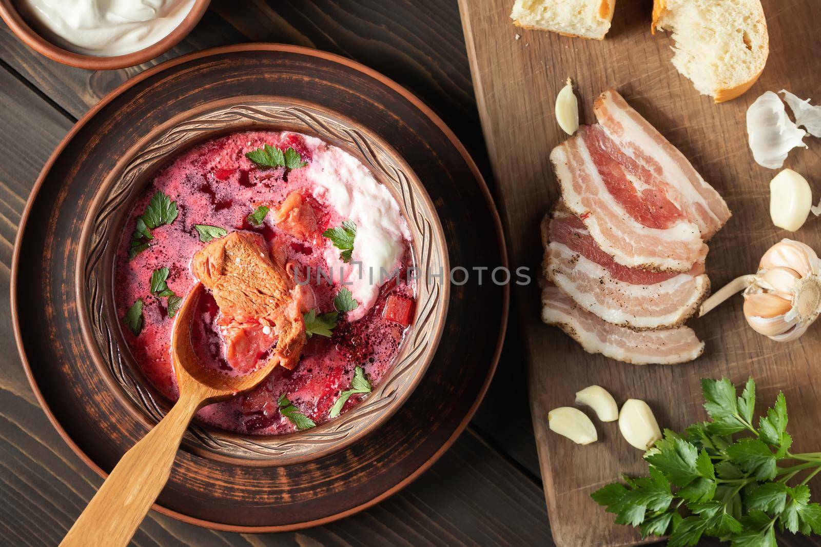 Freshly cooked borscht - traditional dish of Russian and Ukrainian cuisine in earthenware dishes with bacon, bread, sour cream and garlic, top view by galsand