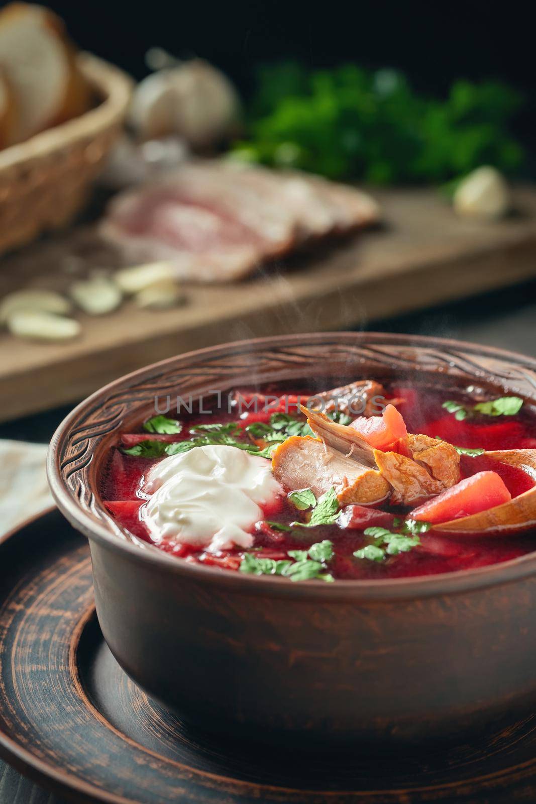 Freshly cooked borscht - traditional dish of Russian and Ukrainian cuisine in earthenware dish with bacon, sour cream and garlic, vertical image by galsand