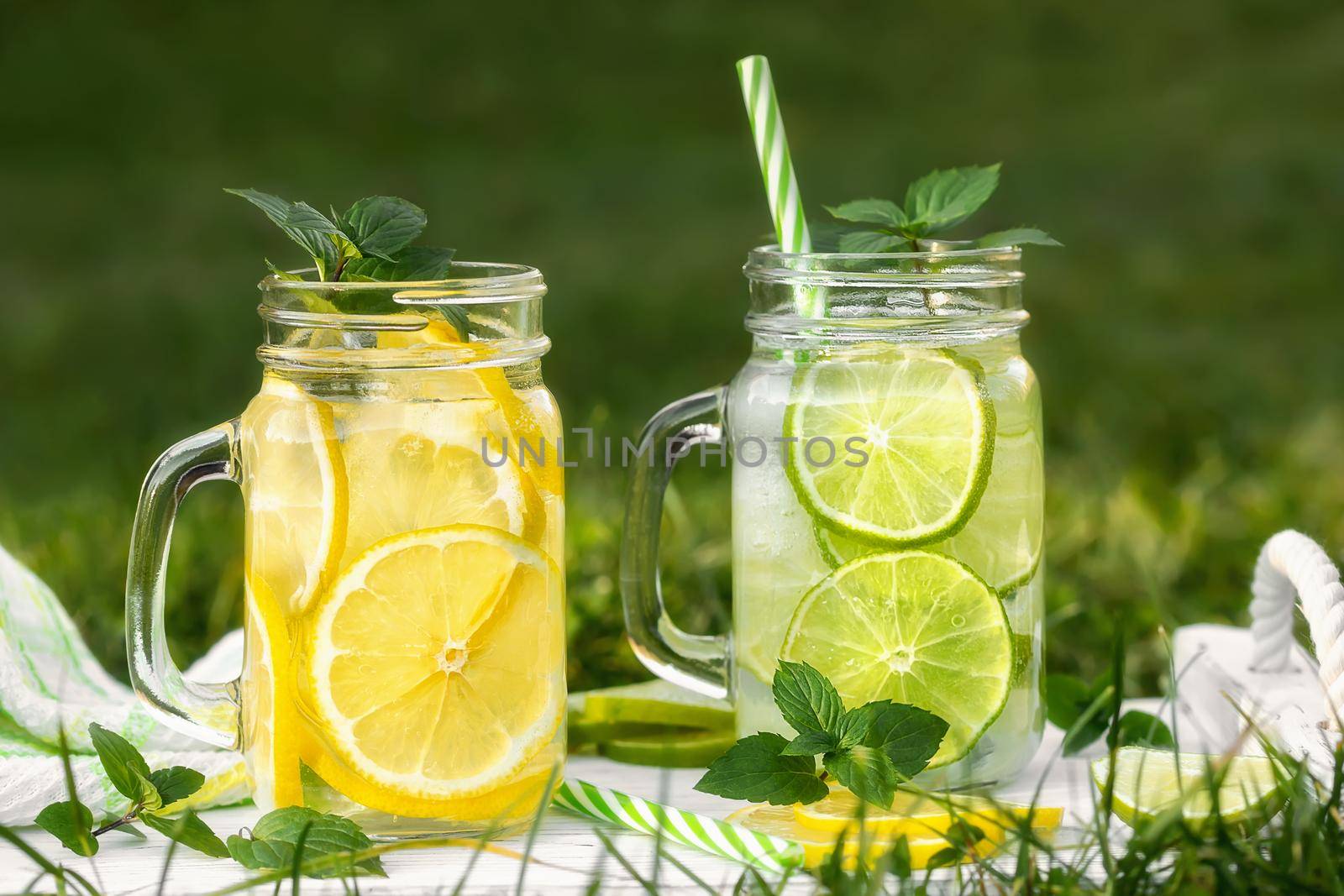 Cold refreshing homemade lemonade with mint, lemon and lime in mason jars on a summer lawn.