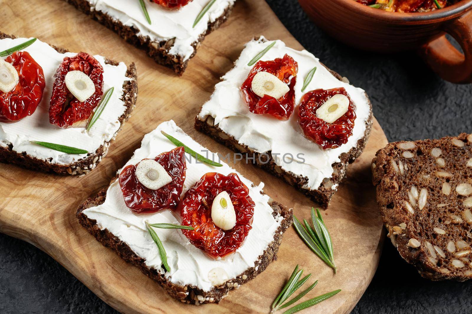 Homemade multigrain bread sandwiches with cream cheese and sun-dried tomatoes on a wooden platter. Healthy eating concept. Flat lay, topview by galsand