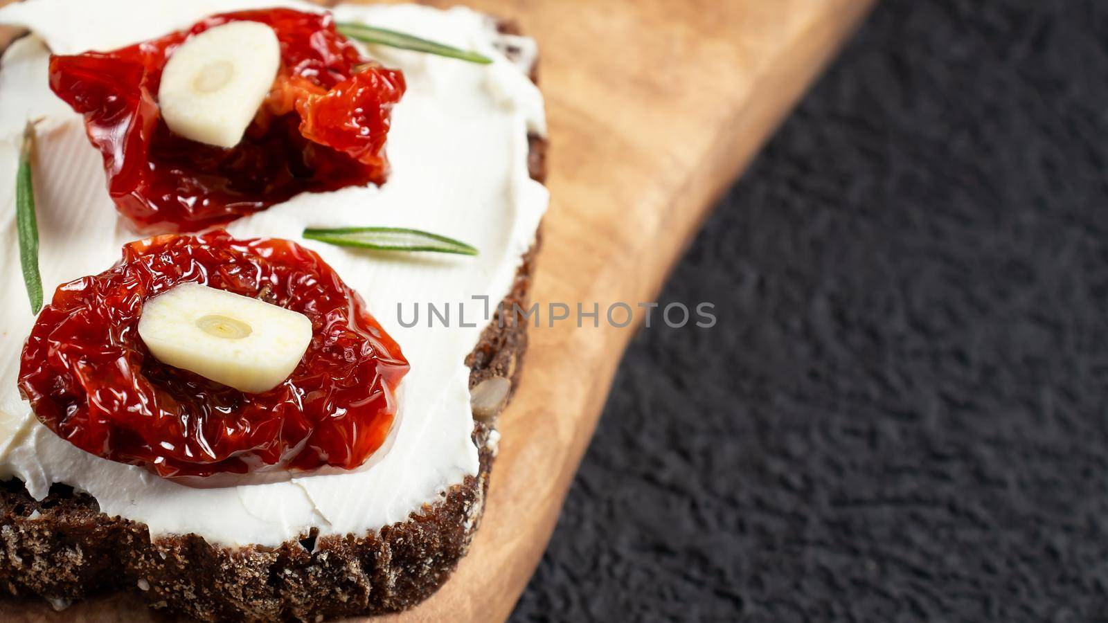 Homemade multigrain bread sandwiches with cream cheese and sun-dried tomatoes on a wooden platter. Healthy eating concept, copy space.