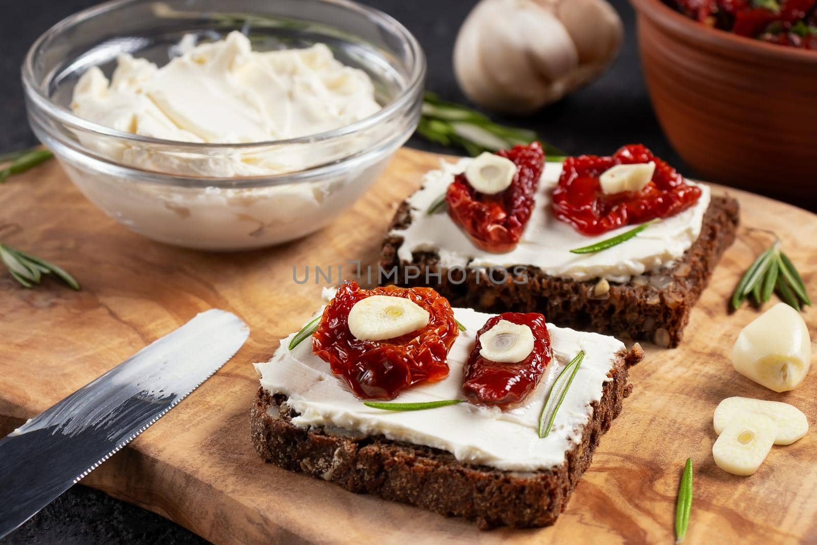 Homemade multigrain bread sandwiches with cream cheese and sun-dried tomatoes on a wooden platter, close-up. Healthy eating concept.