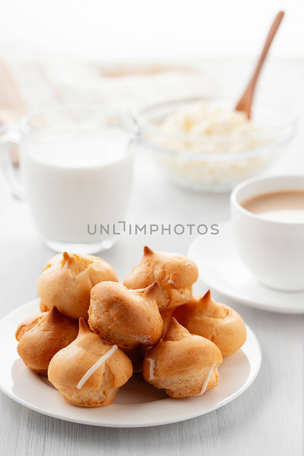 Morning coffee with cakes. Profiteroles, coffee, cream, cottage cheese on a white wooden table. Vertical image.