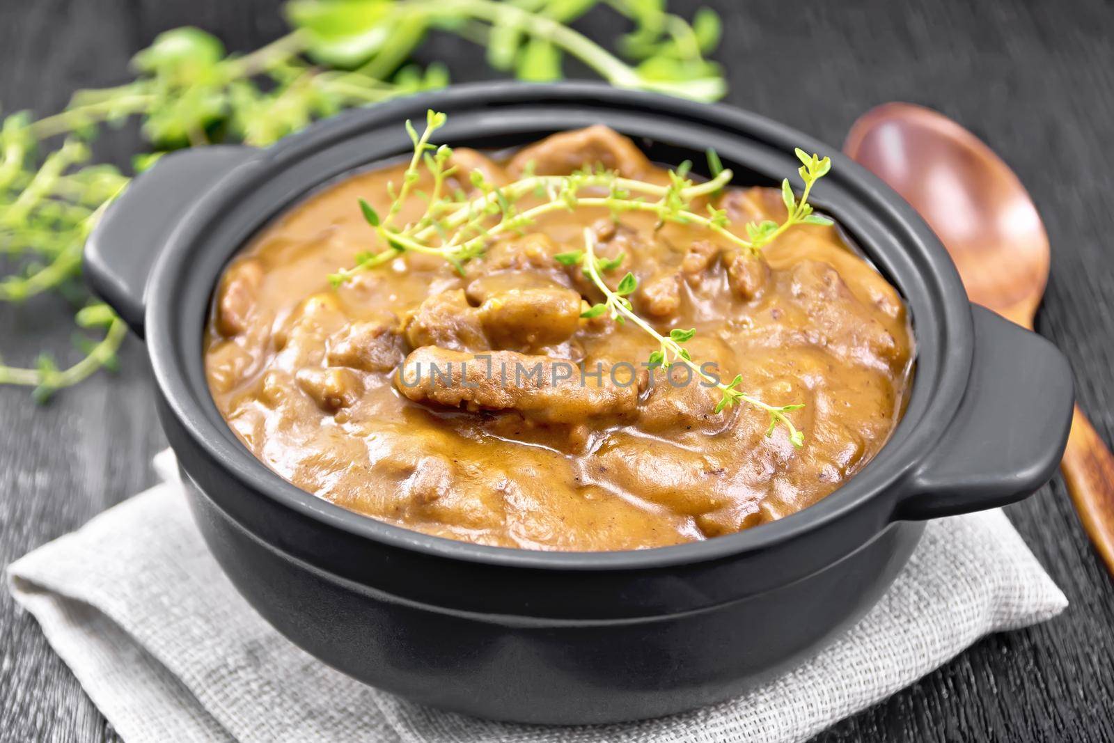 Beef goulash in tomato sauce with sprigs of thyme in a pan on a napkin, spoon, parsley on wooden board background