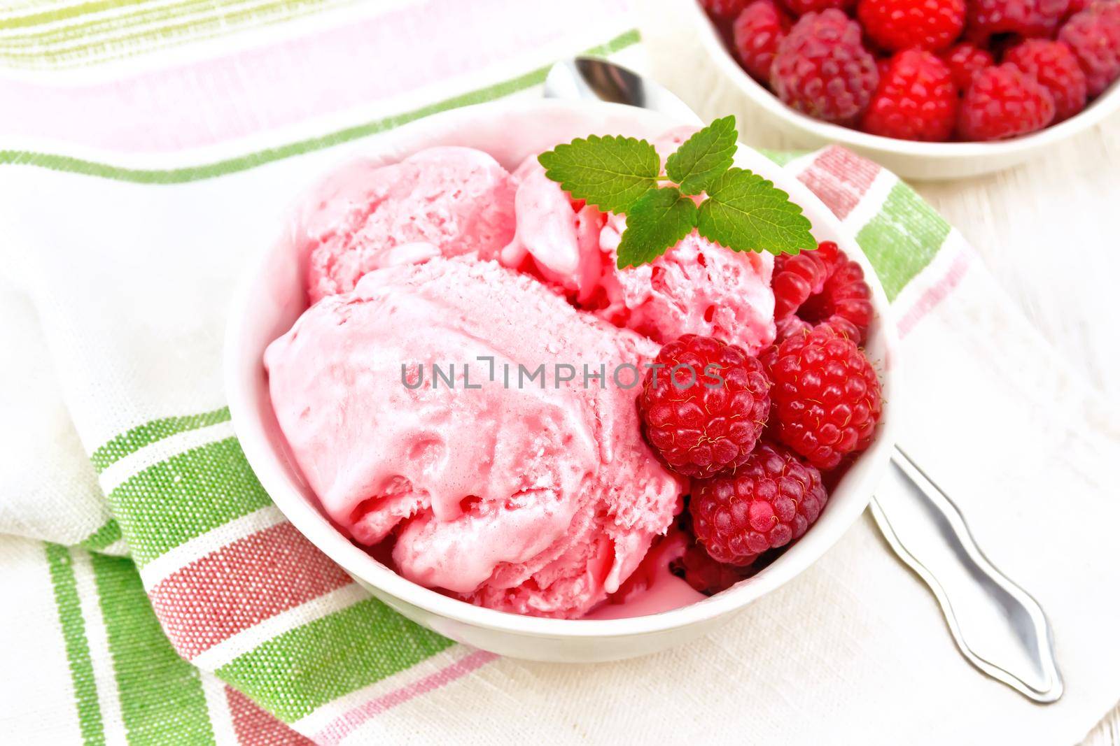 Ice cream crimson with raspberry berries and mint in white bowl, a spoon on napkin on wooden board background