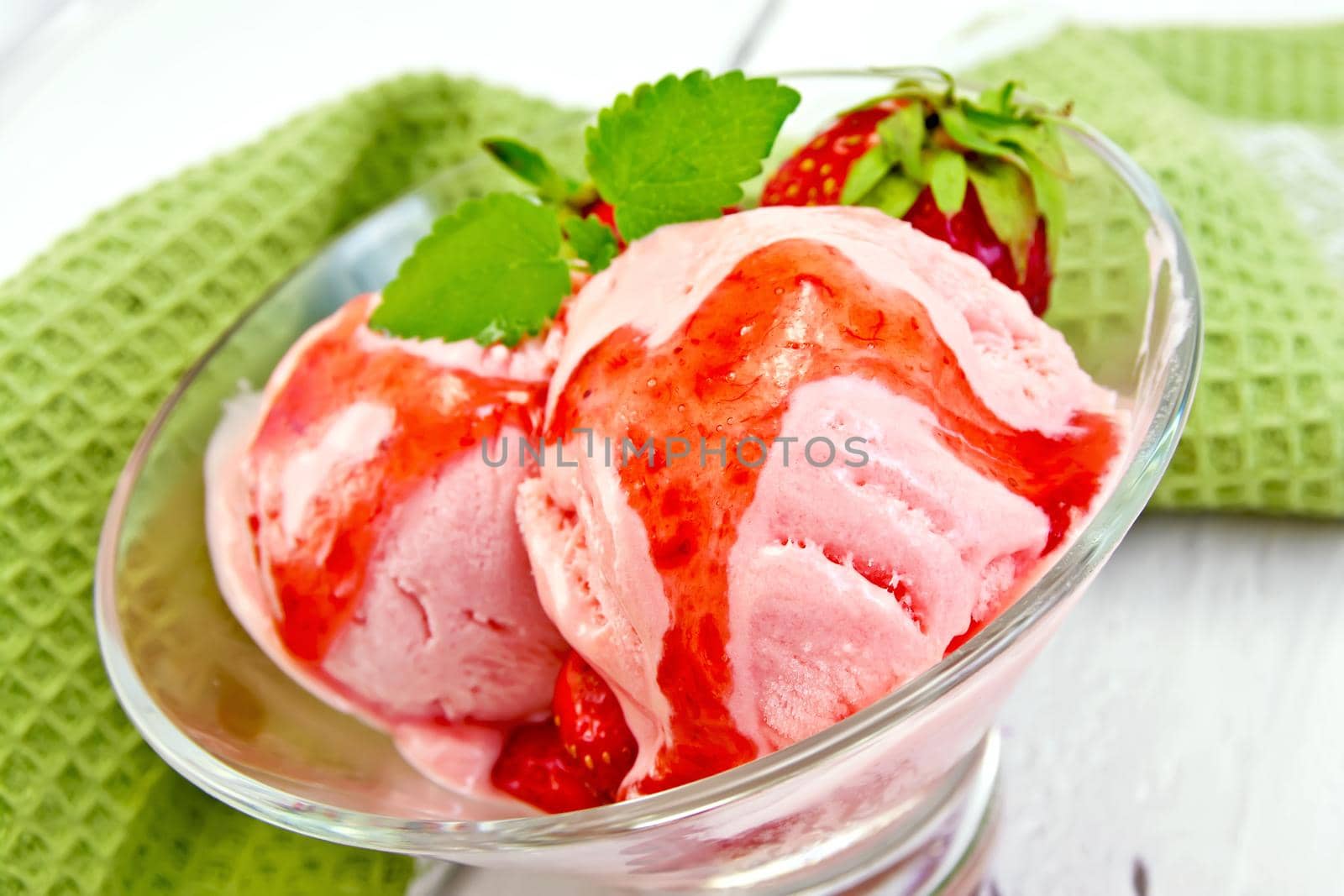 Strawberry ice cream in a glass with strawberries, mint and strawberry syrup, napkin on the background light wooden boards