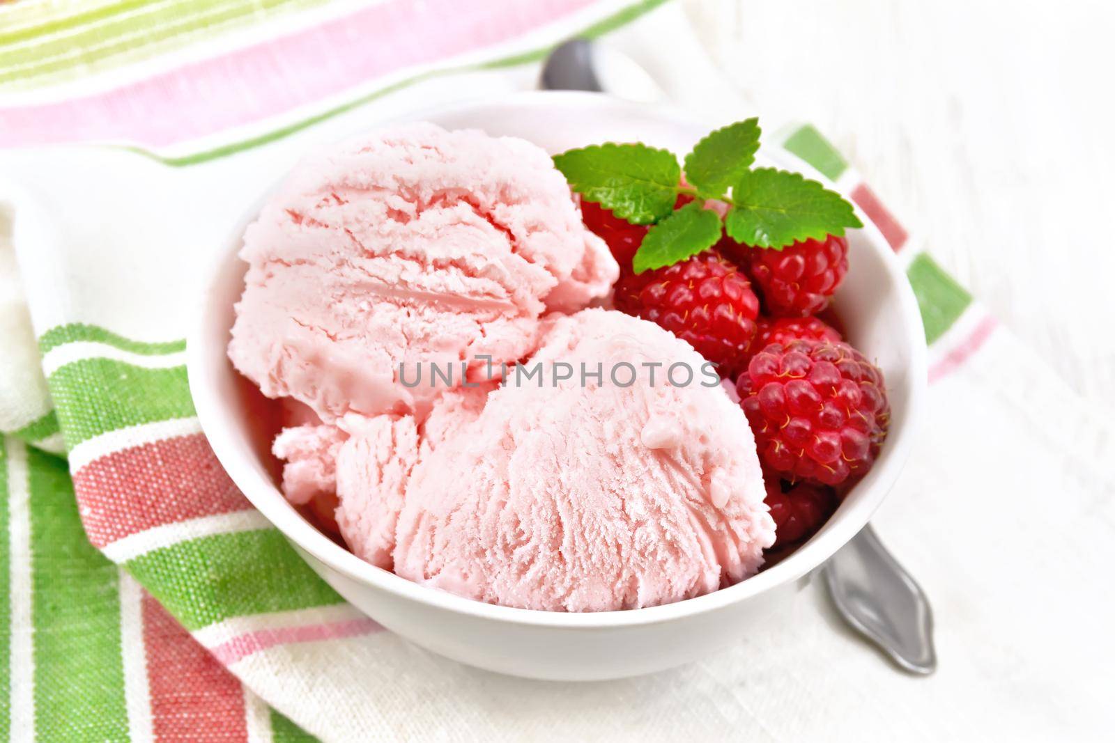 Ice cream crimson with raspberry berries and mint in white bowl, a spoon on towel on the background of wooden board