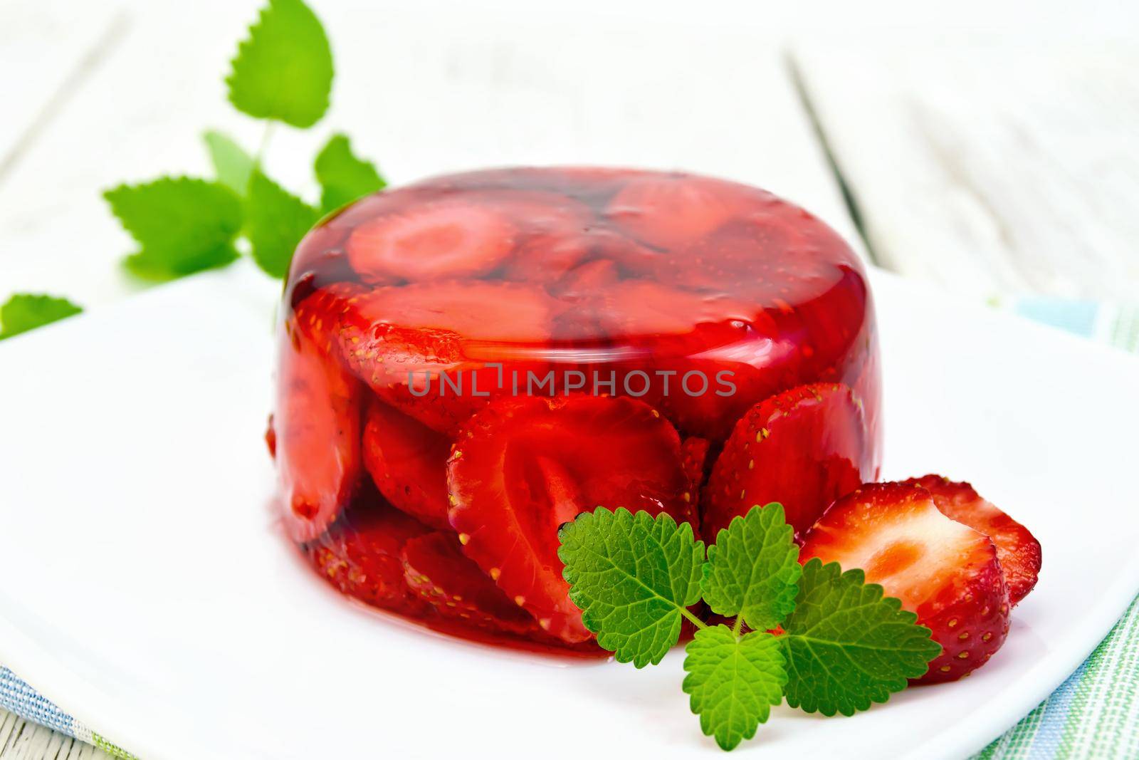 Strawberry jelly with mint and berries in white plate on the kitchen towel on a background of wooden boards