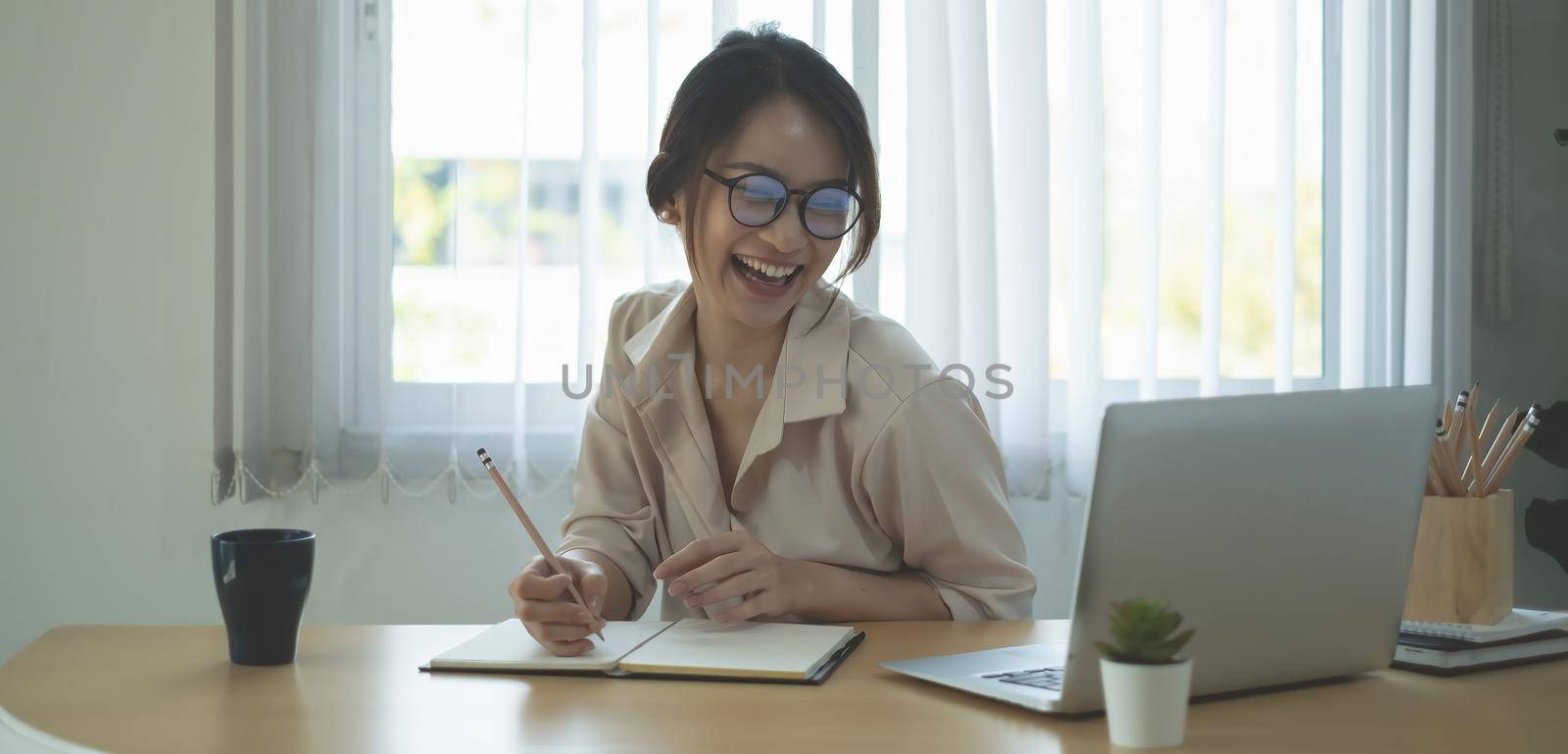 Joyful businesswoman sitting at desk looking at laptop screen talking with friend make video call.