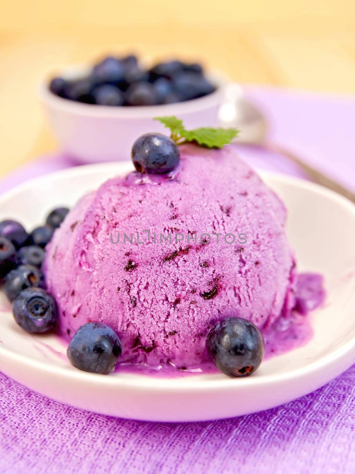Blueberry ice cream with mint and berries in a bowl, a bowl of blueberries on a background of purple cloth and wooden planks