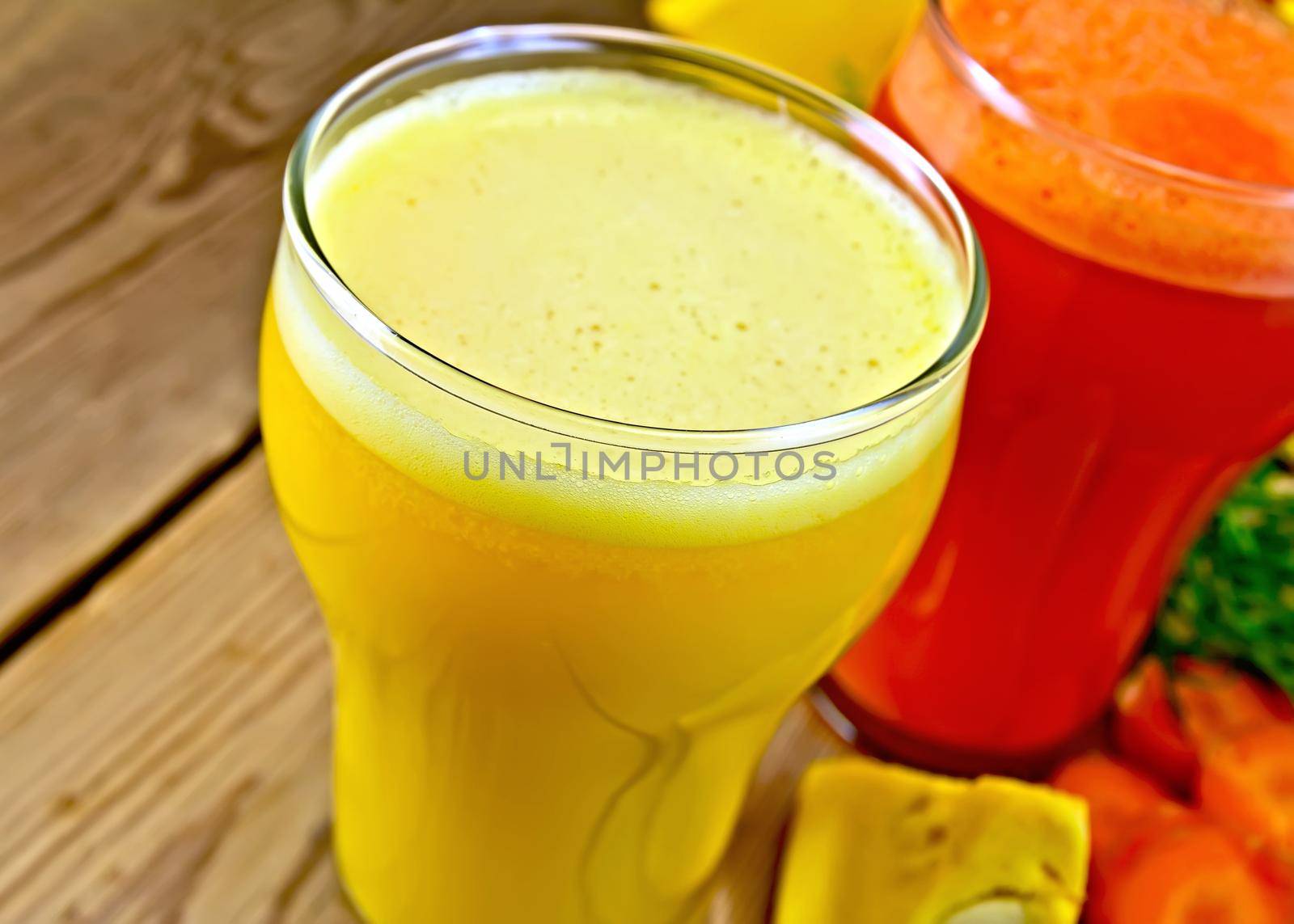 Two tall glasses of pumpkin and carrot juice, vegetables on a wooden boards background