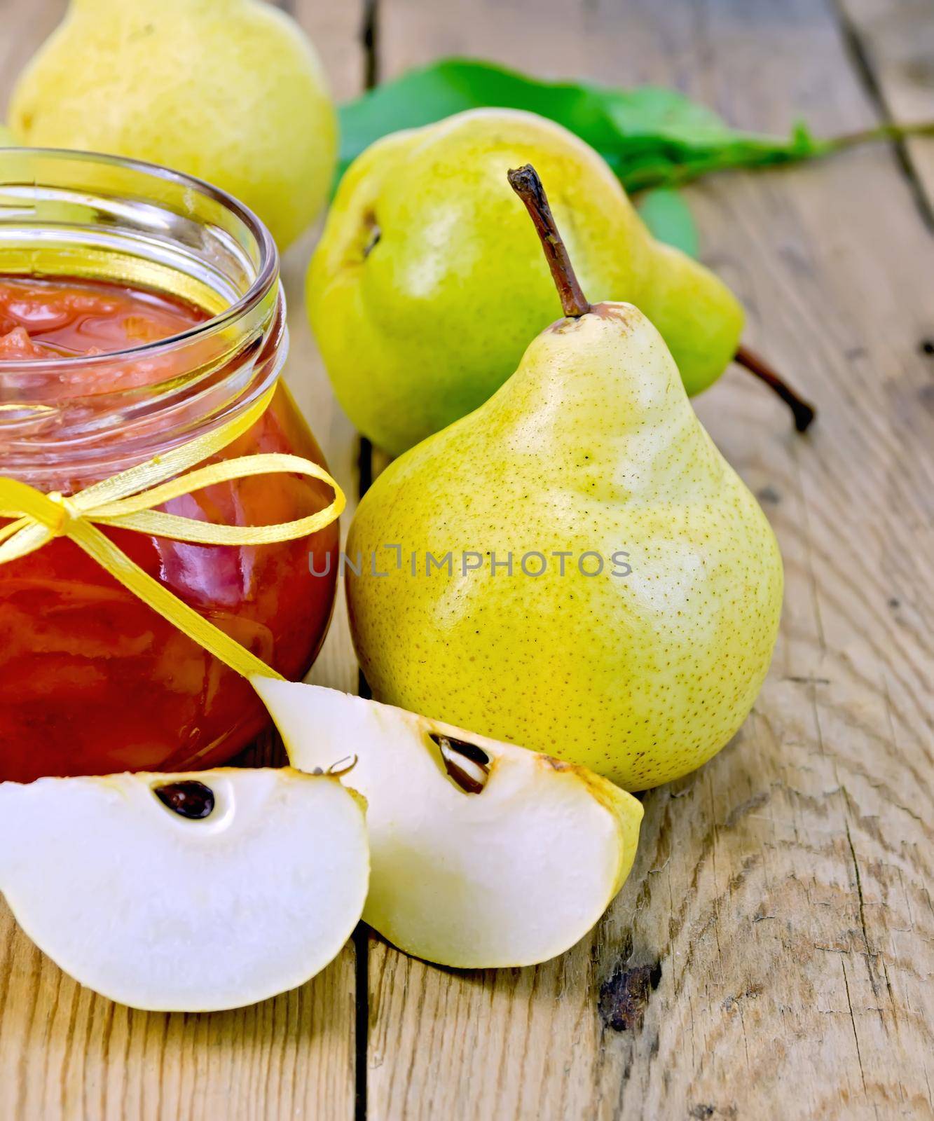 Pear jam in a glass jar, yellow pears whole and slices on a wooden boards background