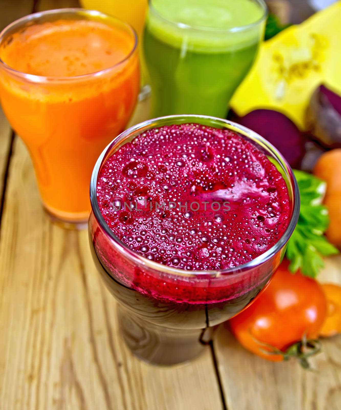 Juice beetroot, carrot, pumpkin and cucumber in a tall glass, vegetables on a wooden boards background