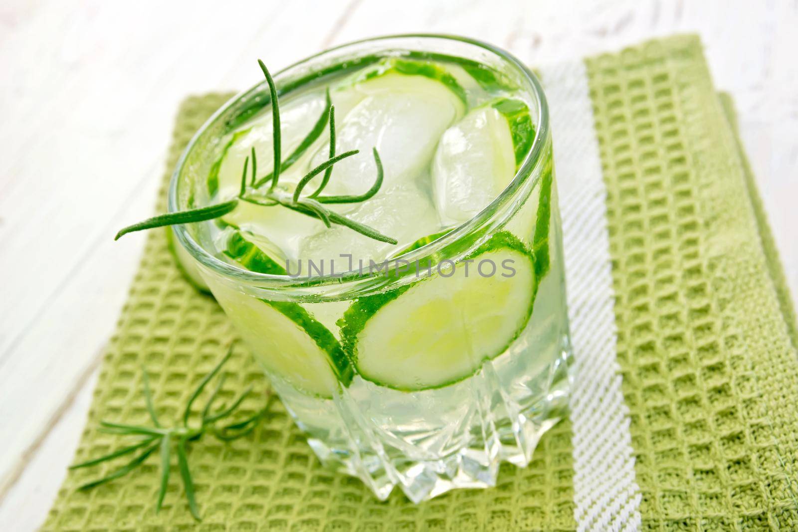 Lemonade with a cucumber and rosemary in a glass on a napkin on a wooden boards background