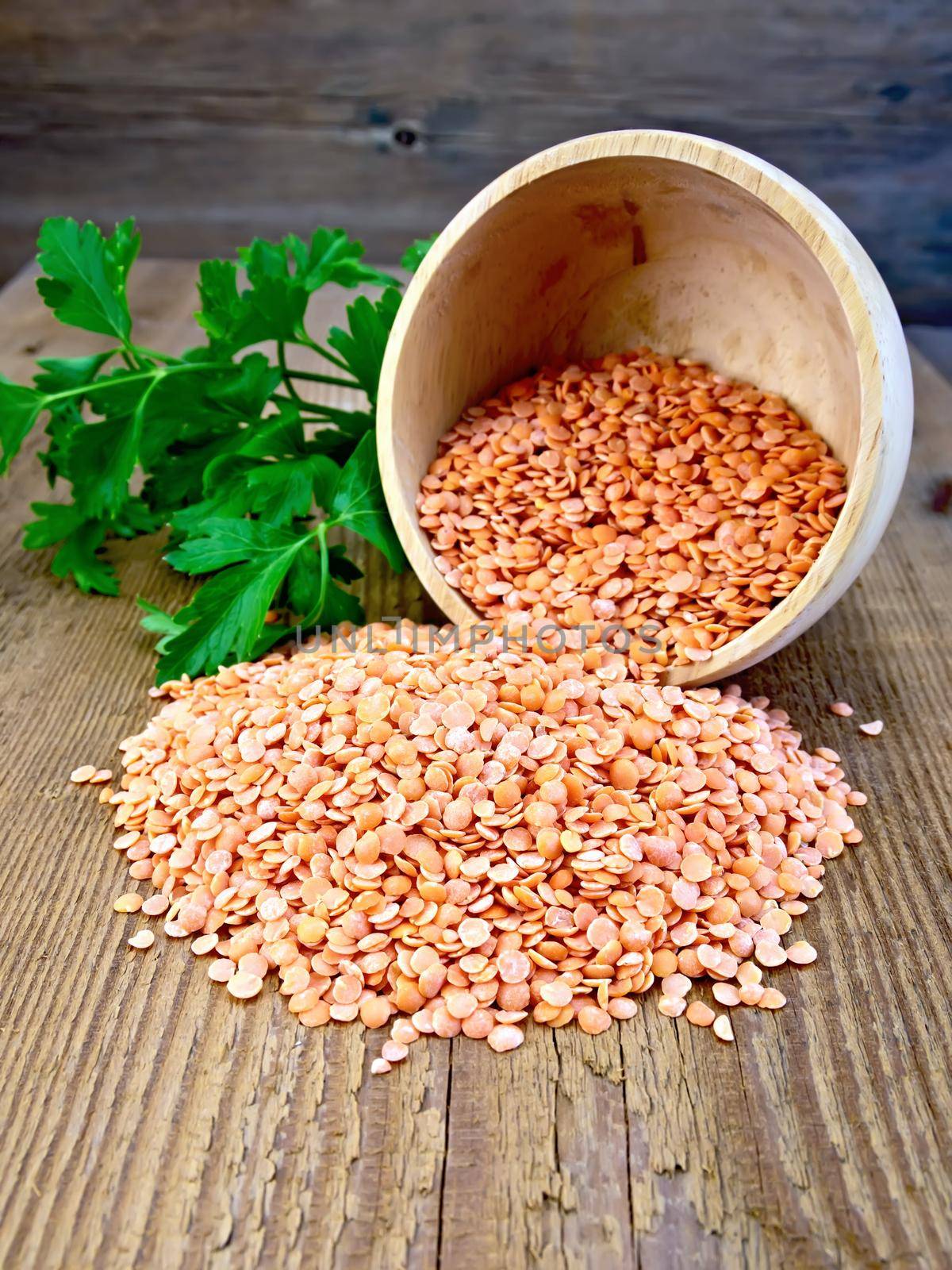 Red lentils in a wooden bowl, parsley on a wooden boards background