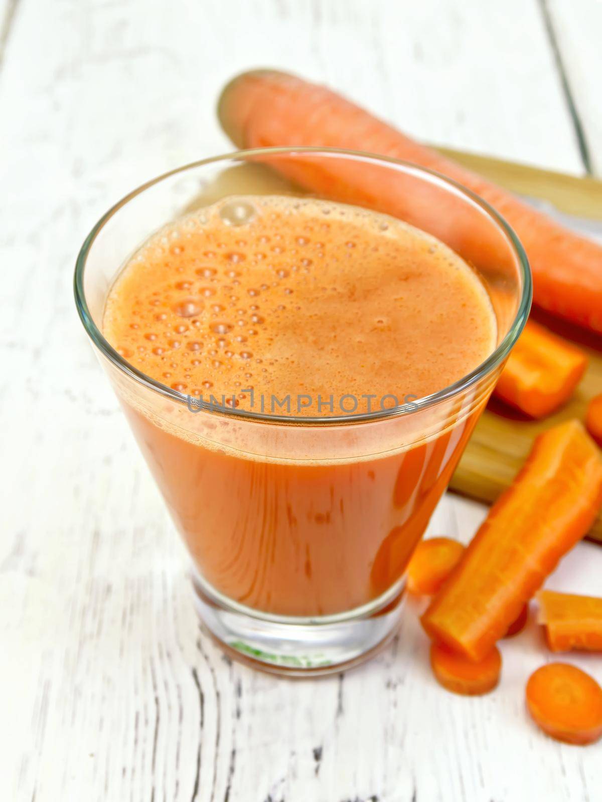 Carrot juice in a tall glass, vegetables on the background of wooden boards