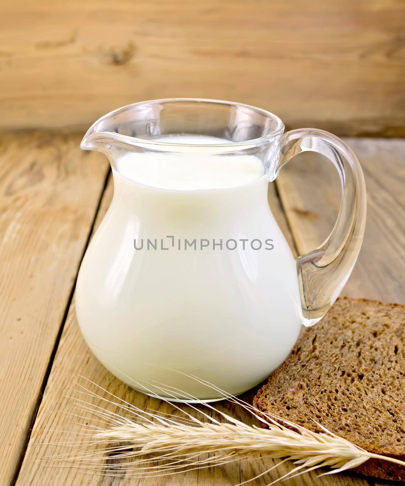 Milk in a glass jar with a slice of bread and spikelet on the background of wooden boards