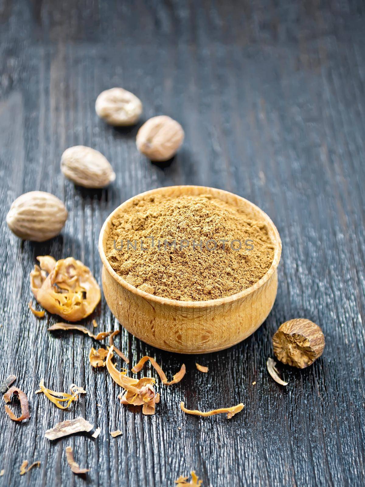 Ground nutmeg in a bowl, dried nutmeg arillus and whole nuts on a black wooden board background