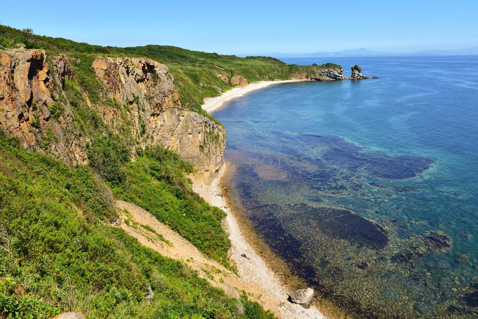 Mountains and seascape with blue sky. Green vegetation in the mountains, sandy beach and amazig sea.