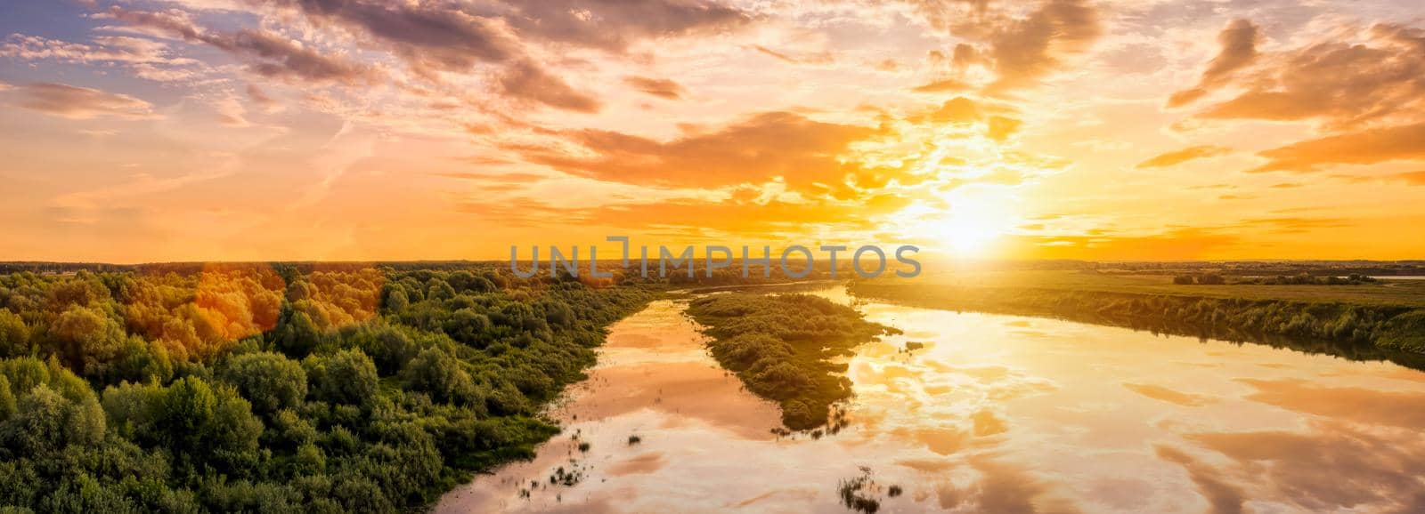 Aerial view to sunset on the river at summer evening with clouds and willow trees. Water reflection of a sky.