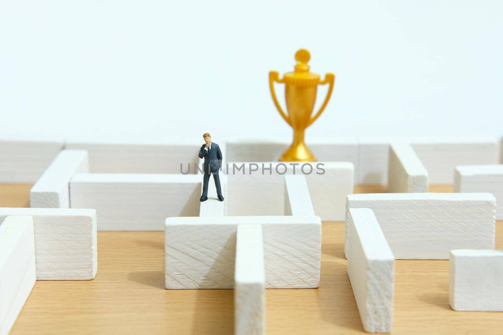 Business strategy conceptual photo - Miniature of businessman on a labyrinth maze seeking the golden trophy. Image photo