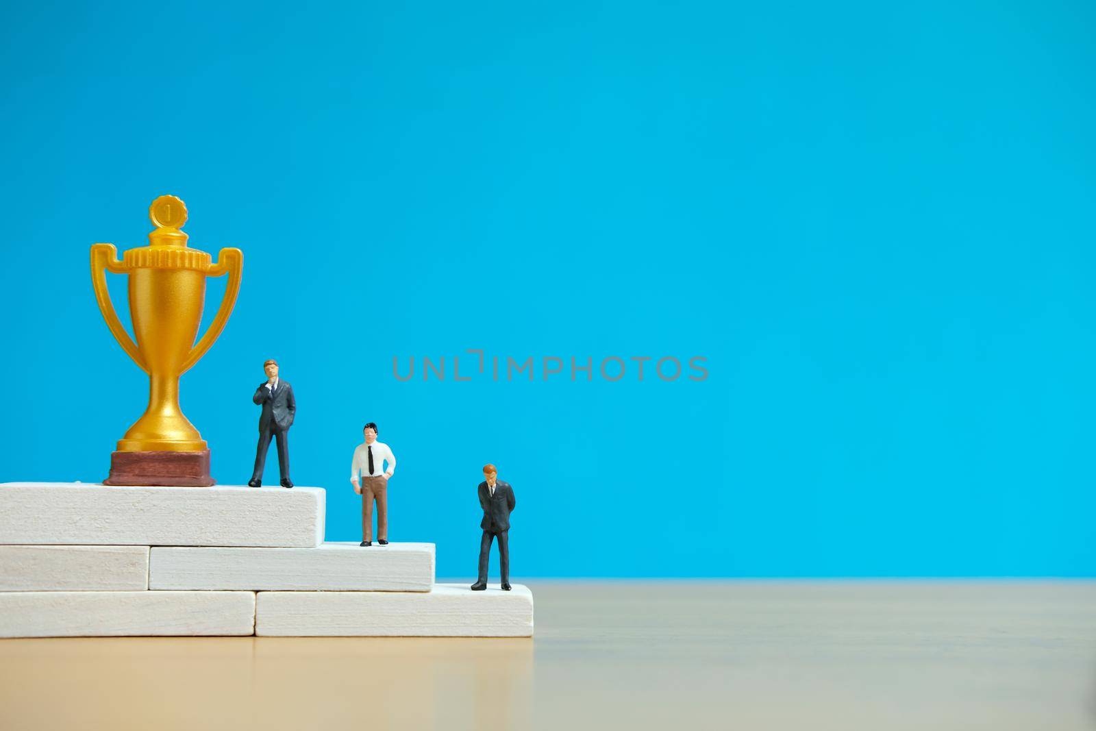 Miniature business concept - businessman standing on white winner podium with golden and silver trophy. Image photo