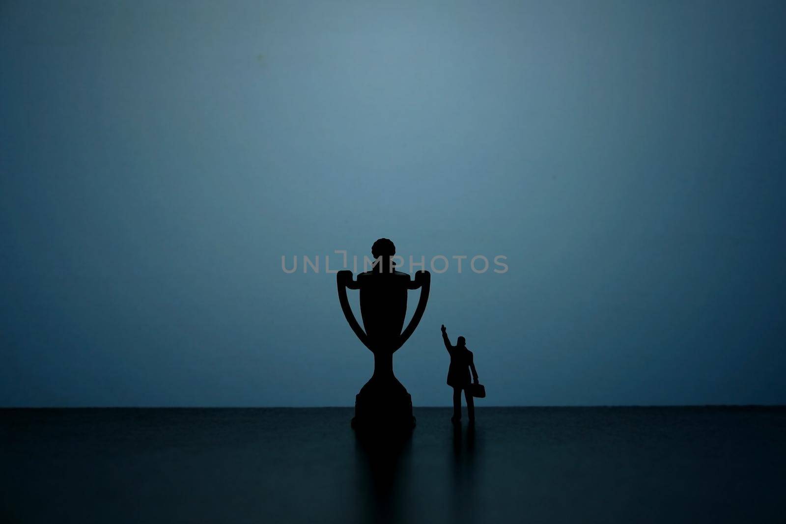 Business strategy conceptual photo - Silhouette of miniature businessman pointing on winning trophy by Macrostud