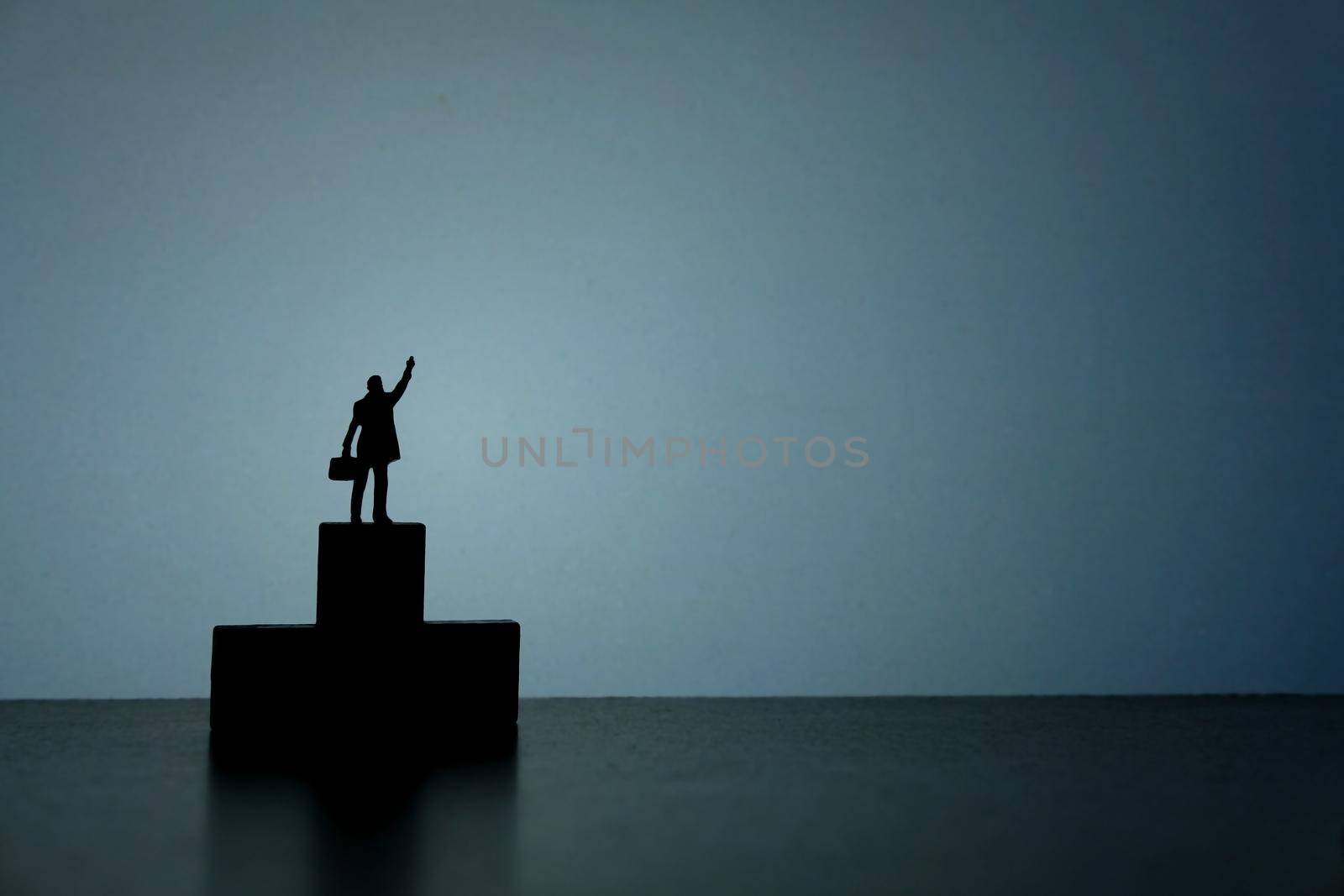 Business strategy conceptual photo - Silhouette of miniature businessman standing on podium while pointing upside by Macrostud