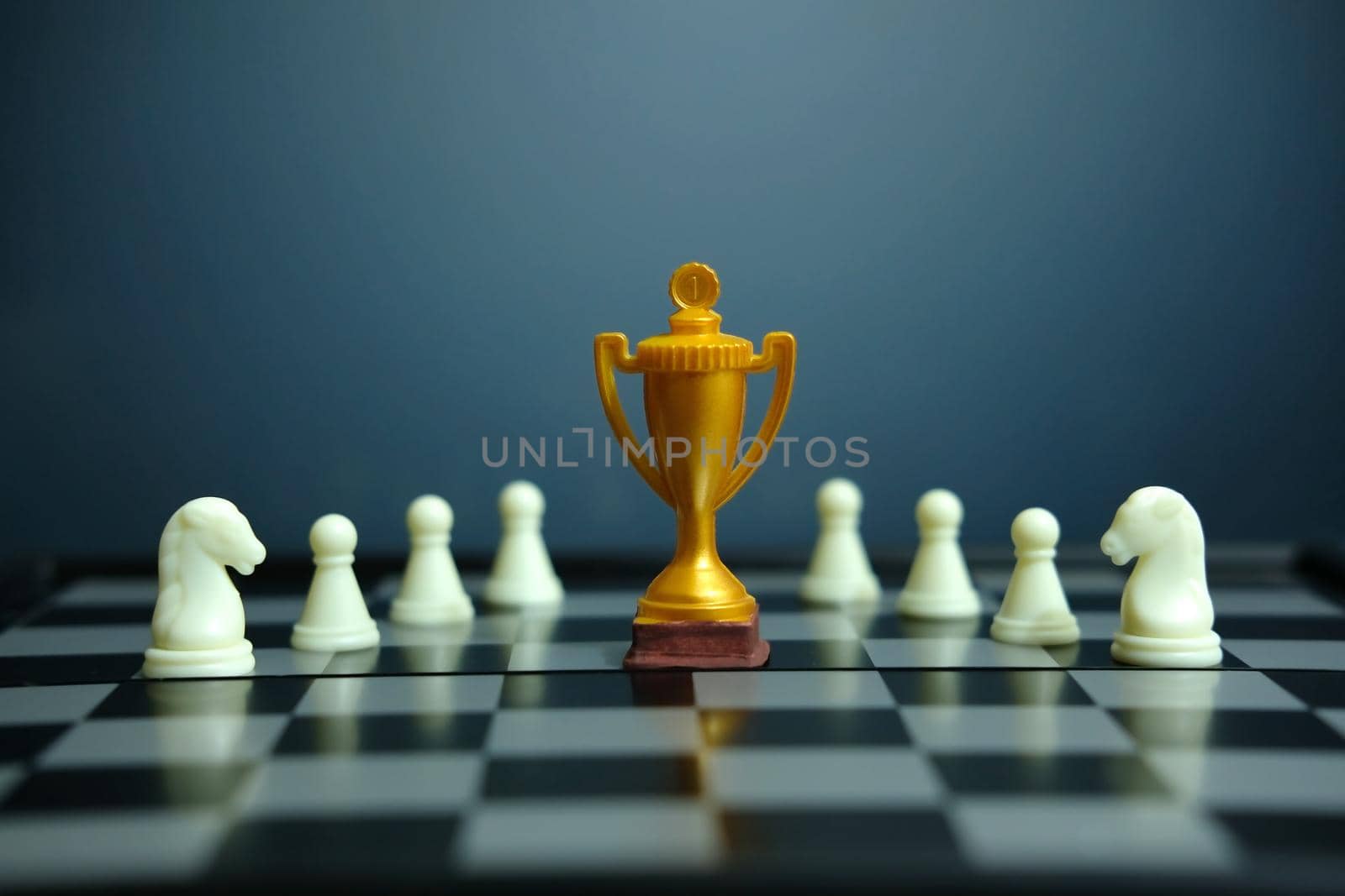 Business strategy conceptual photo – Golden trophy standing on chessboard with chess pawn. Image photo