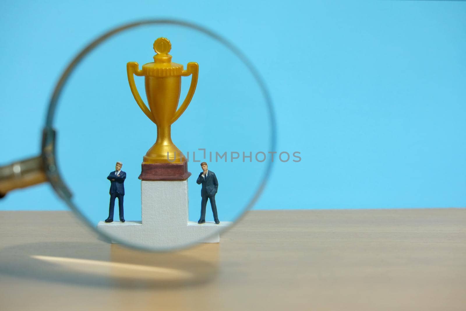 Miniature business concept - businessman standing in front of white podium with golden trophy and magnifier glass. Image photo