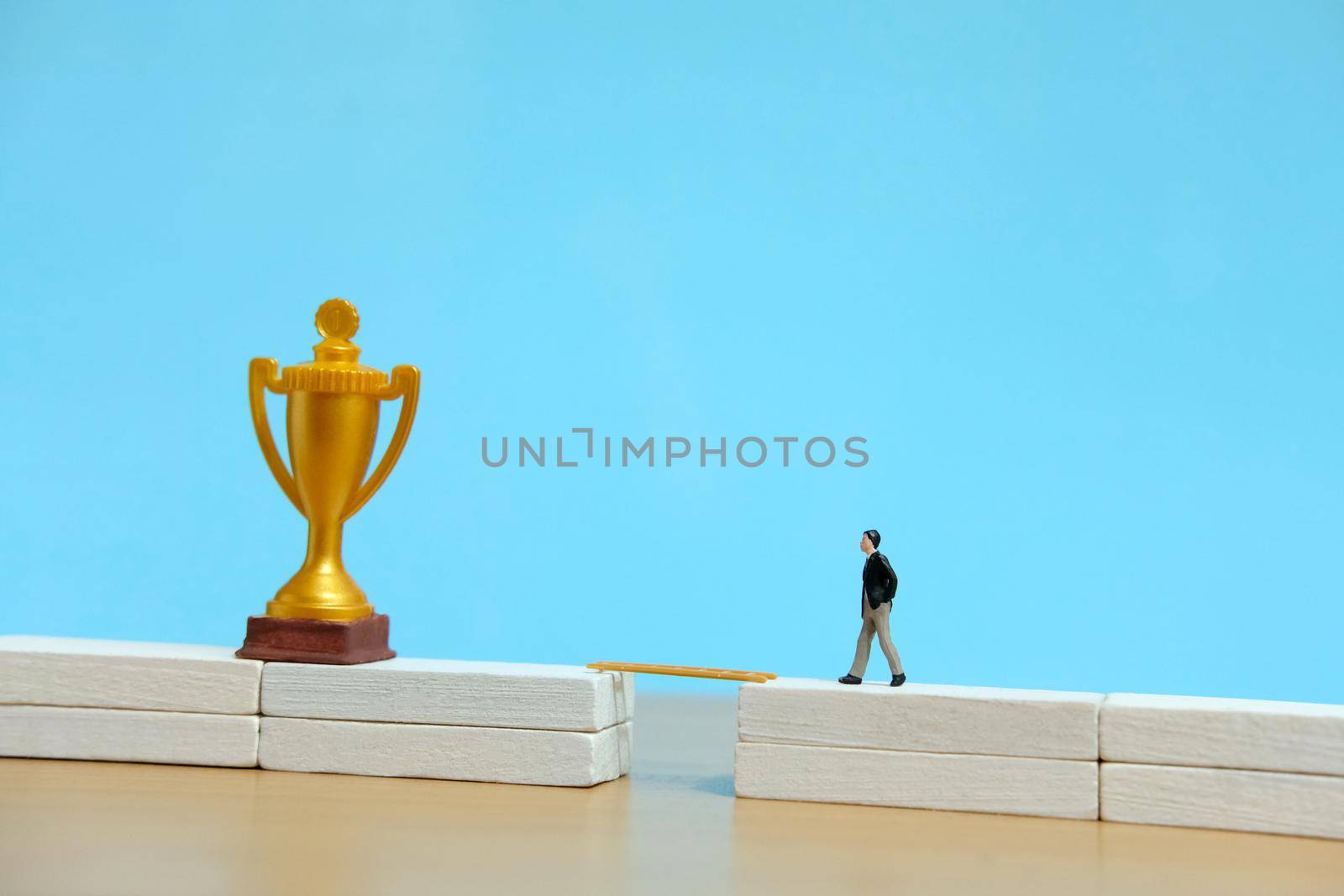 Miniature business concept - businessman walking toward golden trophy above white bridge. Image photo