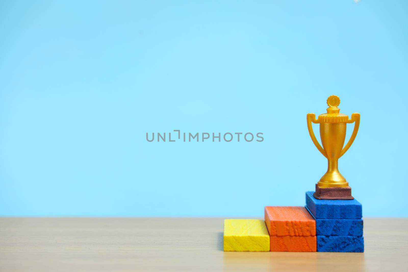 Golden trophy standing at colorful podium on wooden table. Image photo