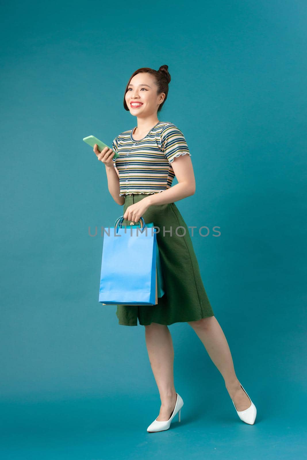Smiling young Asian woman with shopping colour bags over blue background.
