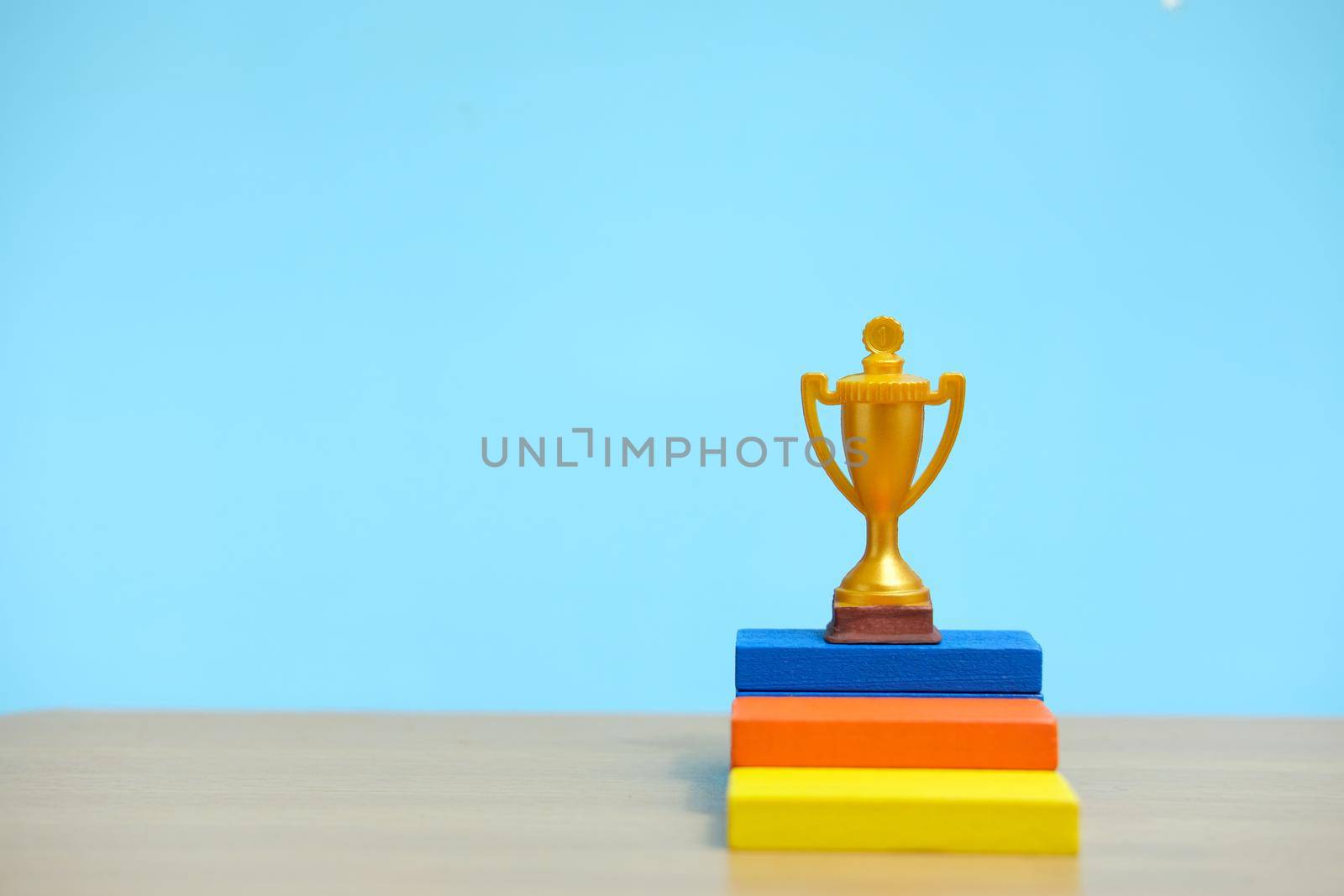 Golden trophy standing at colorful podium on wooden table. Image photo