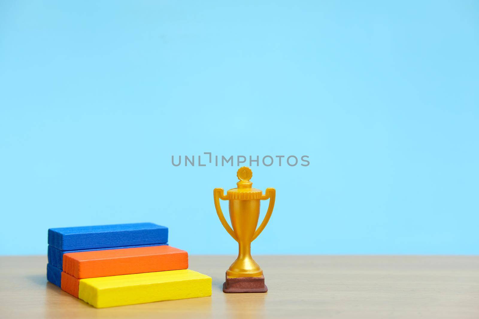 Golden trophy standing beside colorful podium on wooden table. Image photo