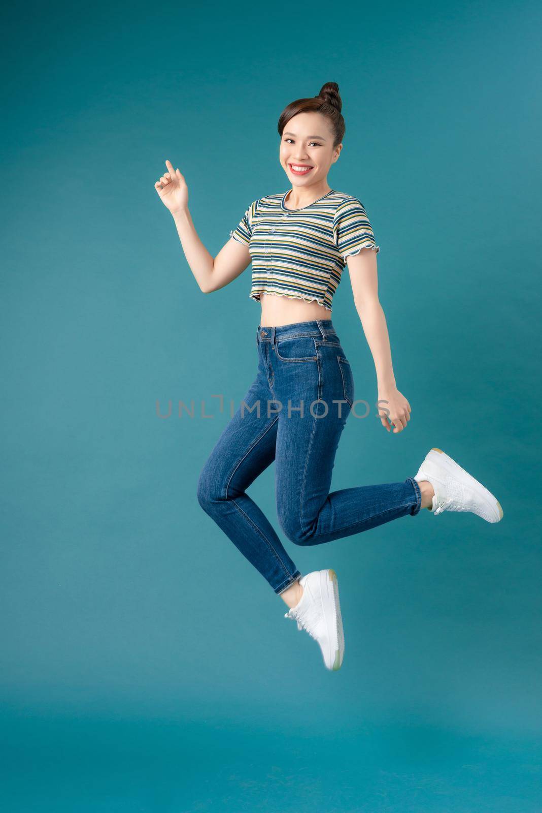 Mischievous girl wearing striped T-shirt and jeans dancing on blue background by makidotvn