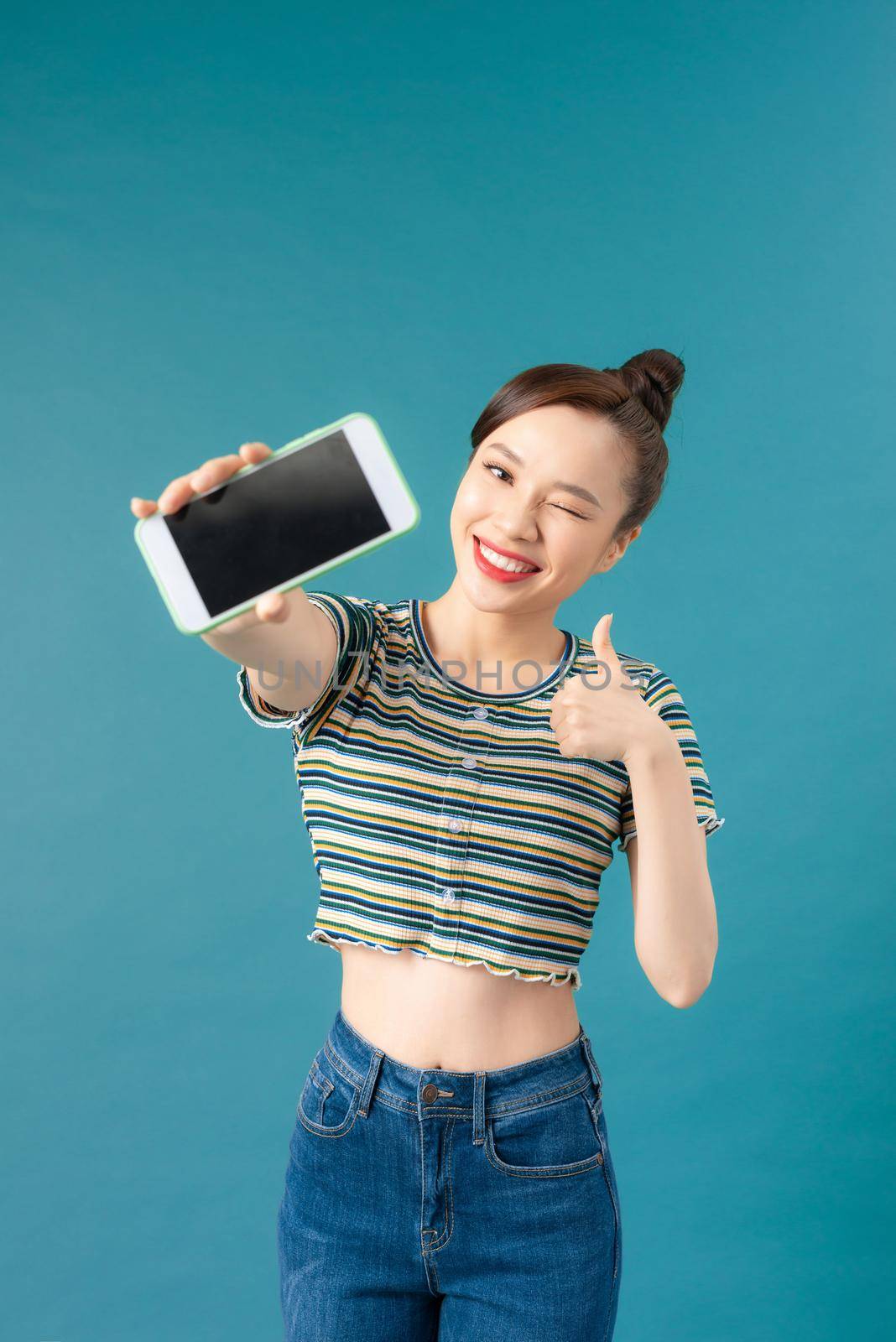 Young Asian woman show thumb up with mobile phone on blue background