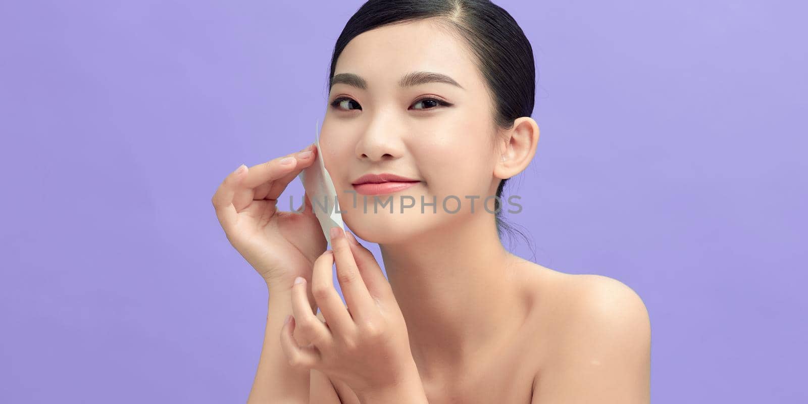 Smiling woman using facial oil blotting paper portrait by makidotvn