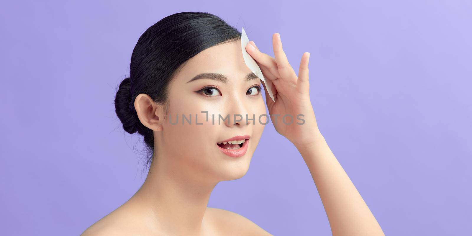 Asian woman using absorbing blotting sheets to remove excess oil on oily face
