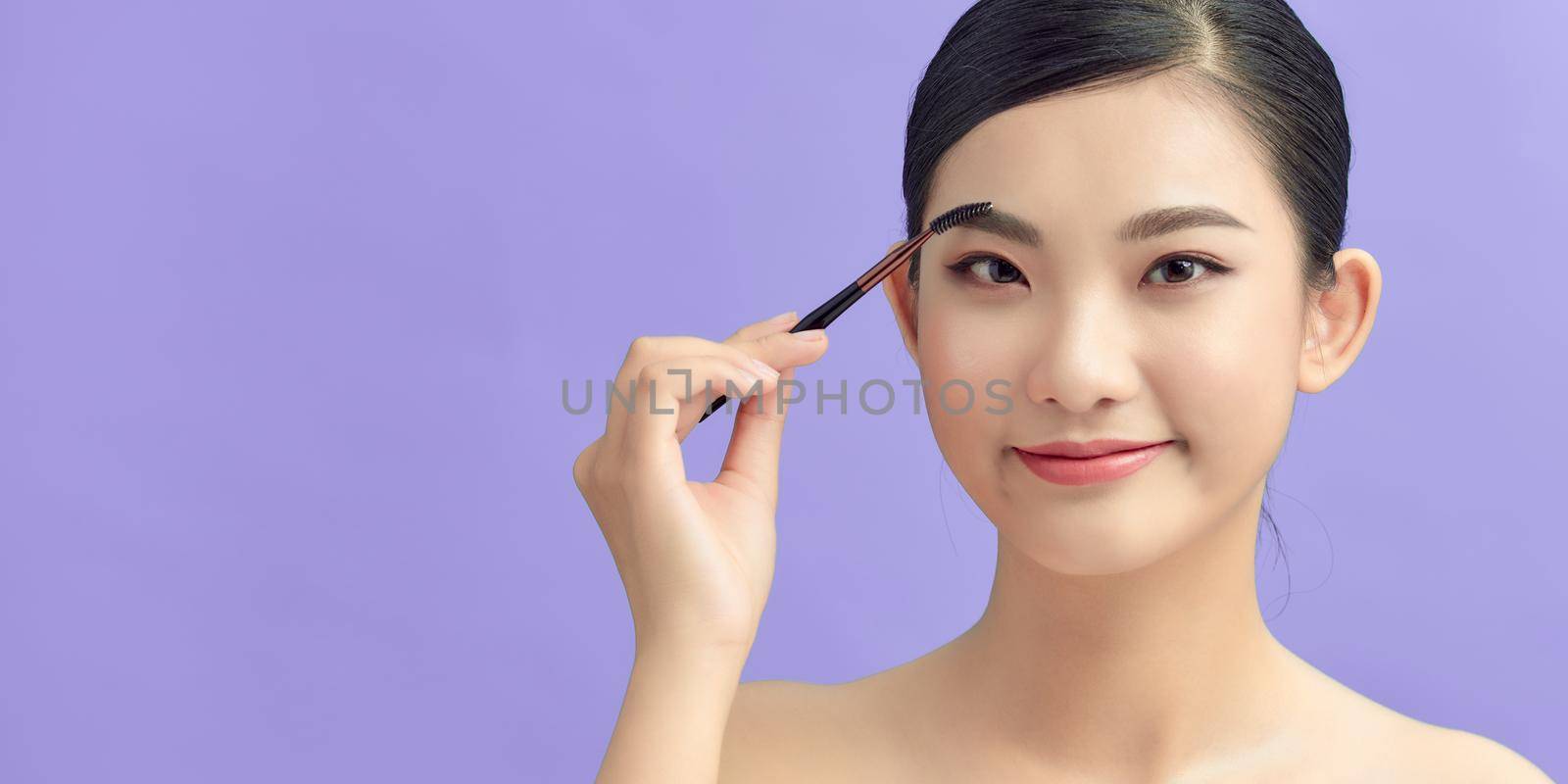 Closeup beautiful woman with eyebrow brush tool on purple