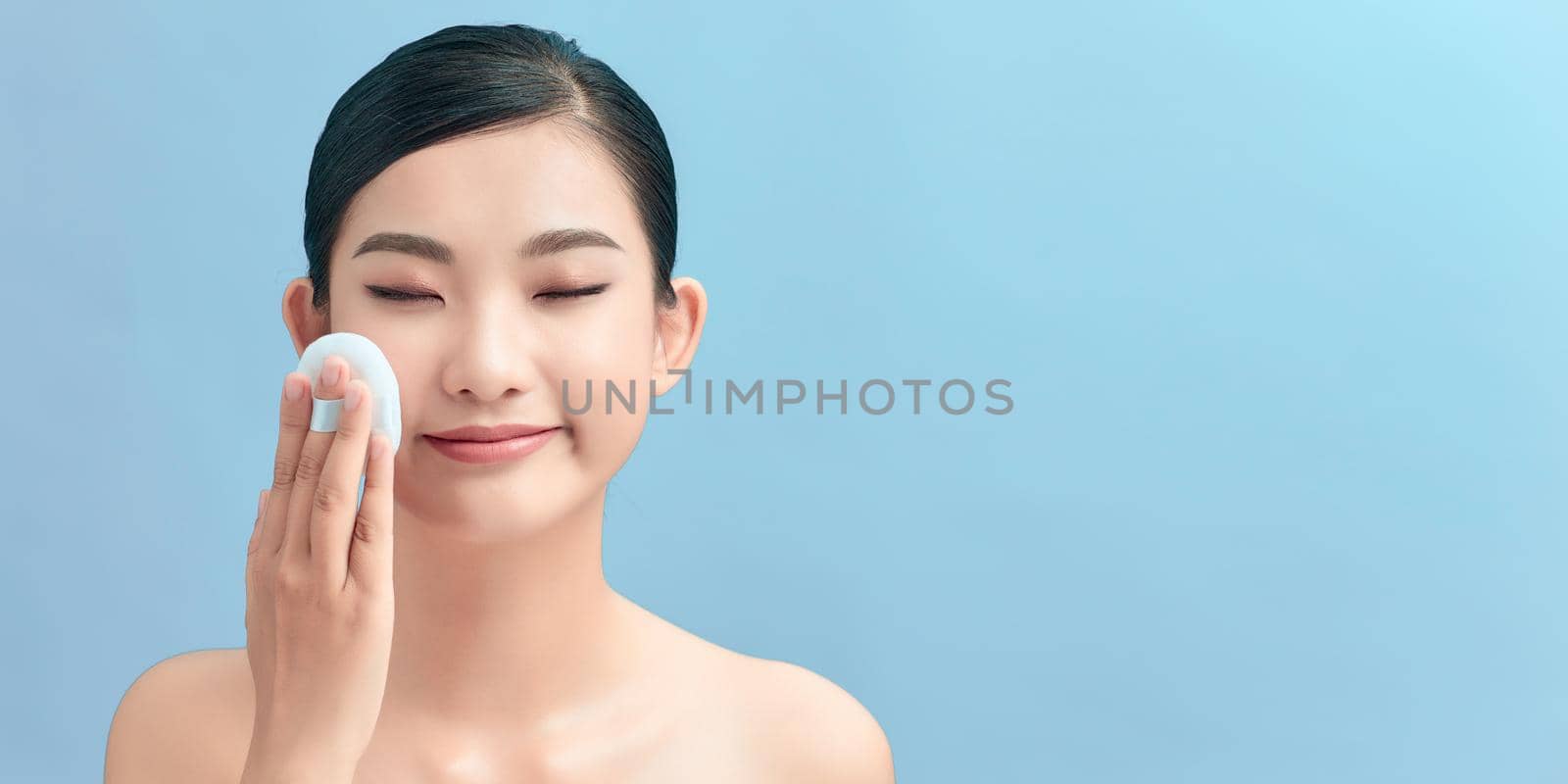 Beautiful woman applying dry powder using cosmetic cushion on her facial skin. by makidotvn