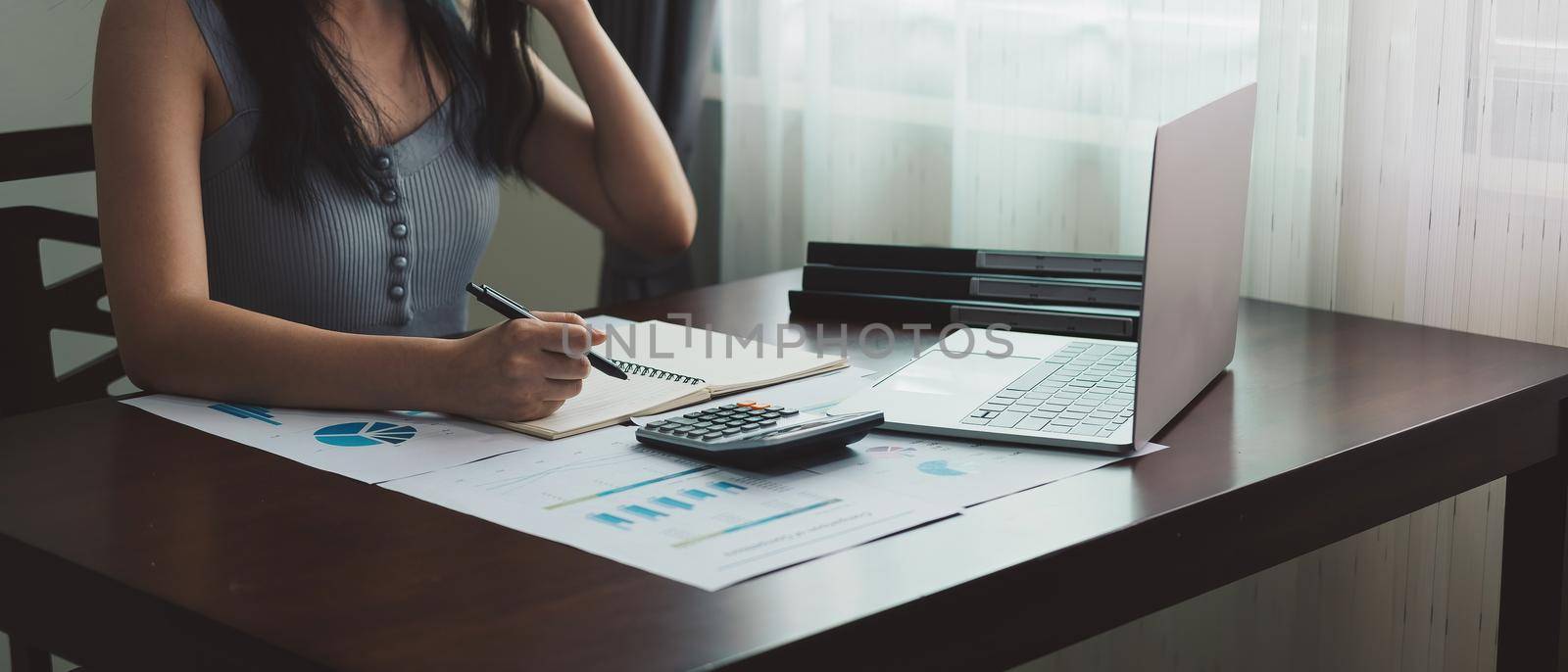 Woman hand is writing on a notebook with a pen for accounting financial at home.