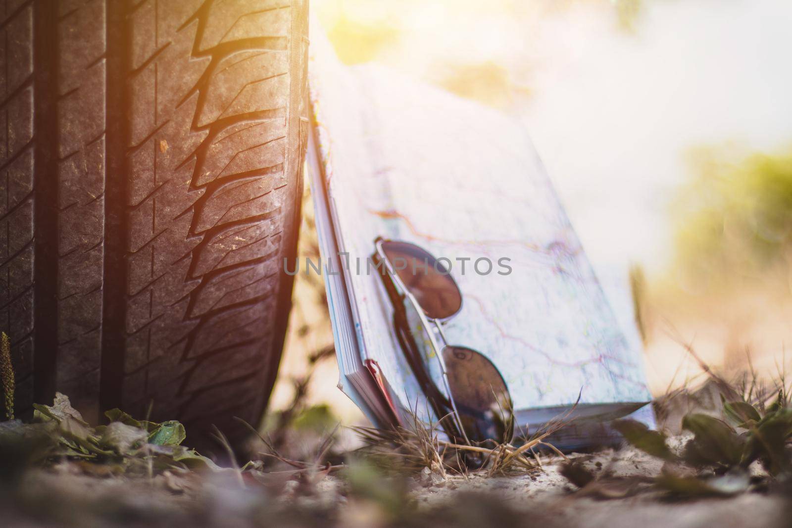 Car tire, sunglasses and roadmap on sandy ground, desert