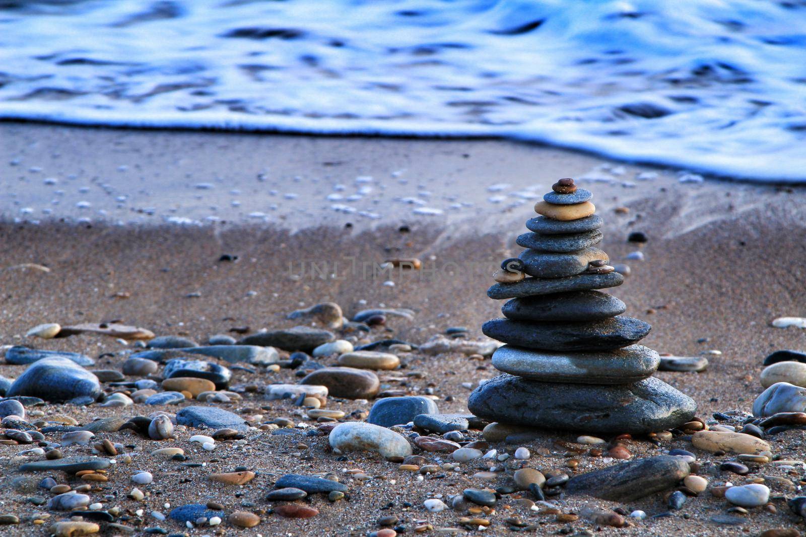 Round stacked stones on the Isla Plana beach at sunset in Cartagena. Waves in the background.