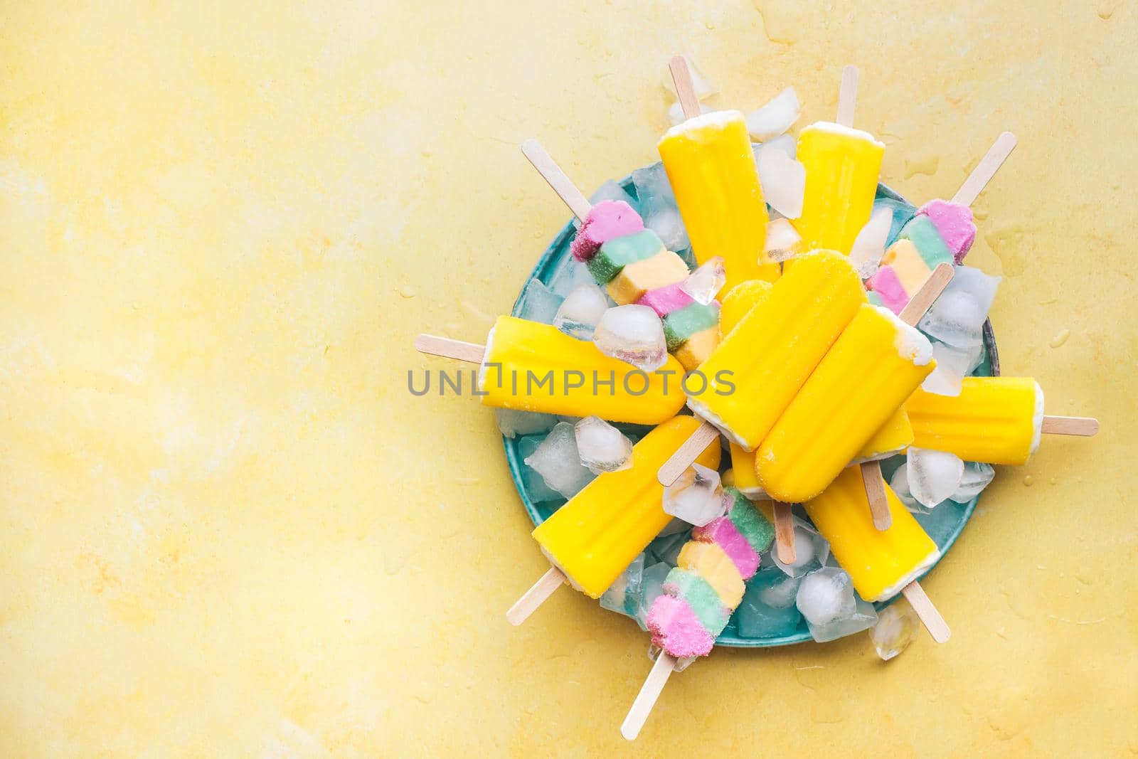 Summer refreshing popsicles on plate of ice cubes on yellow background.  Top view, blank space