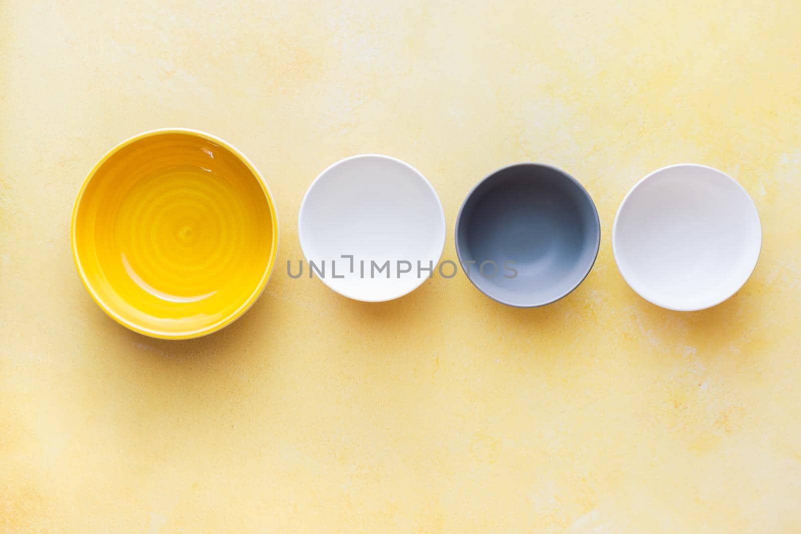 Assorted ceramic multicolored empty bowls on rustic yellow surface. Top view, blank space by Slast20