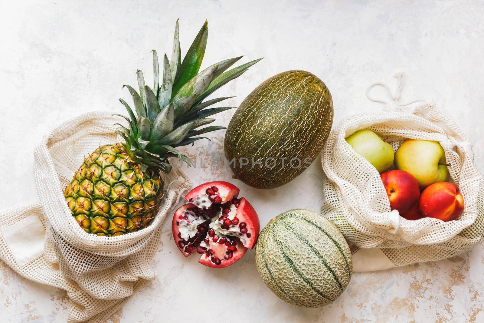 Fresh seasonal fruits (pineapple, green apples, pomegranate, peaches and melon) in eco friendly and reusable shopping mesh bags. Healthy vegan food. Zero waste. Top view, blank space